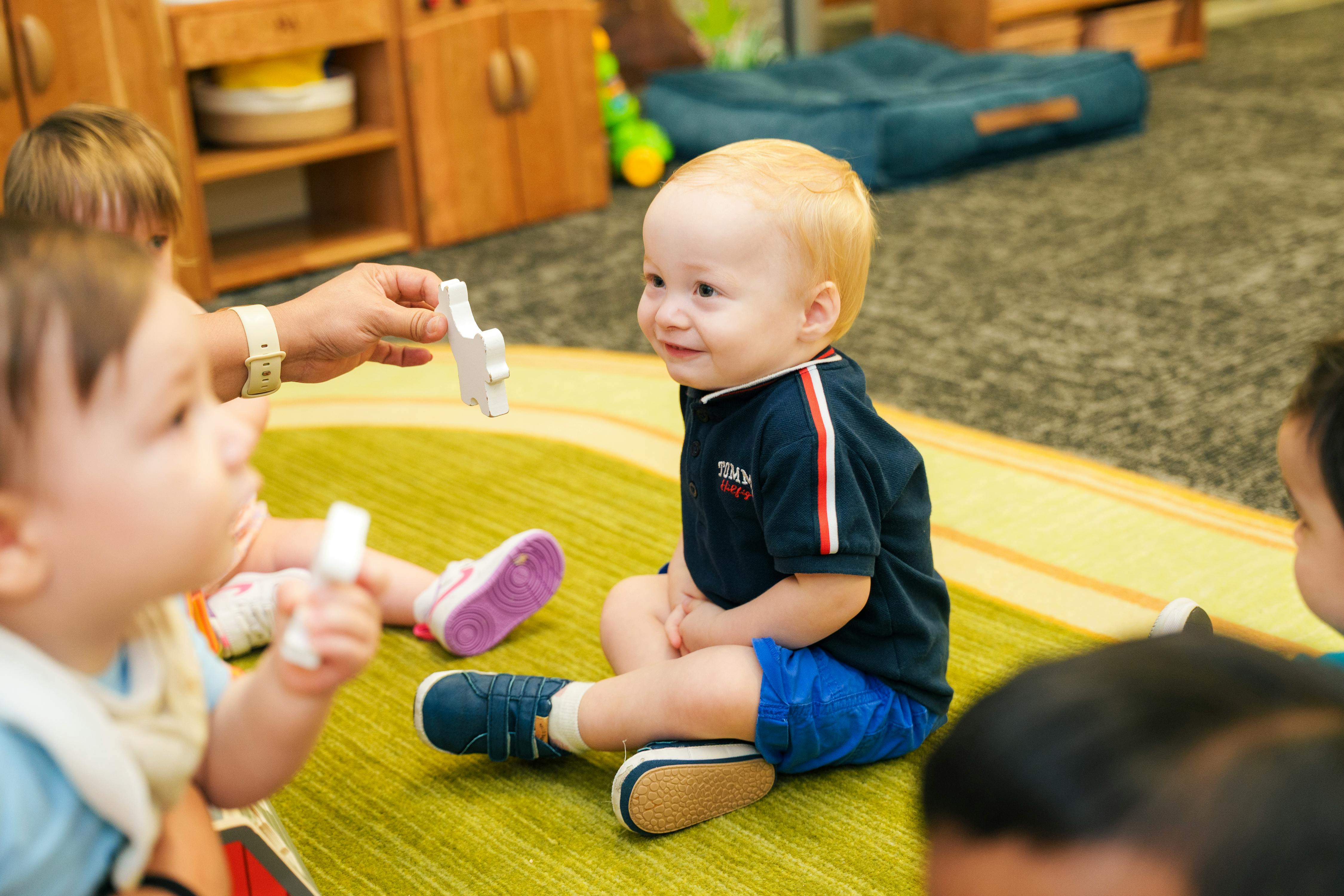 Adult hand offering toy to child sitting on floor with other children