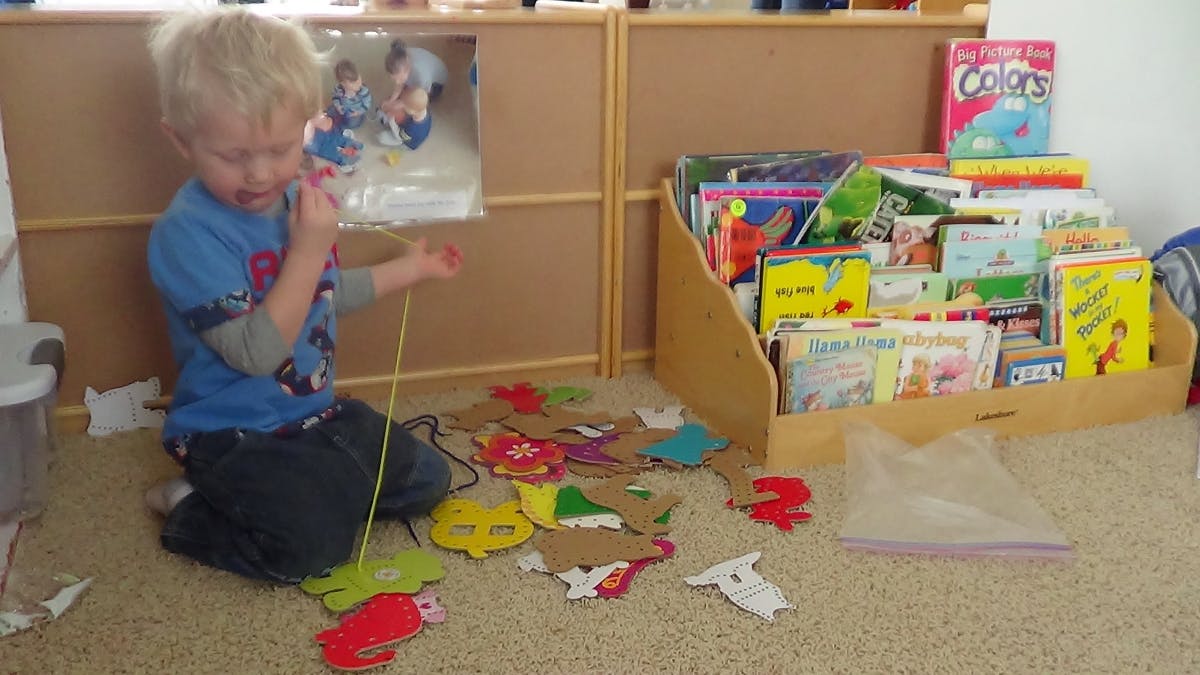 Child playing with string and cutouts on the floor
