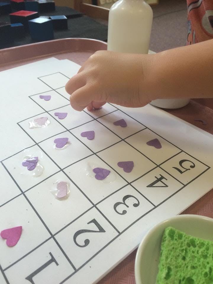 Child's hand placing heart-shaped pieces on a numbered grid