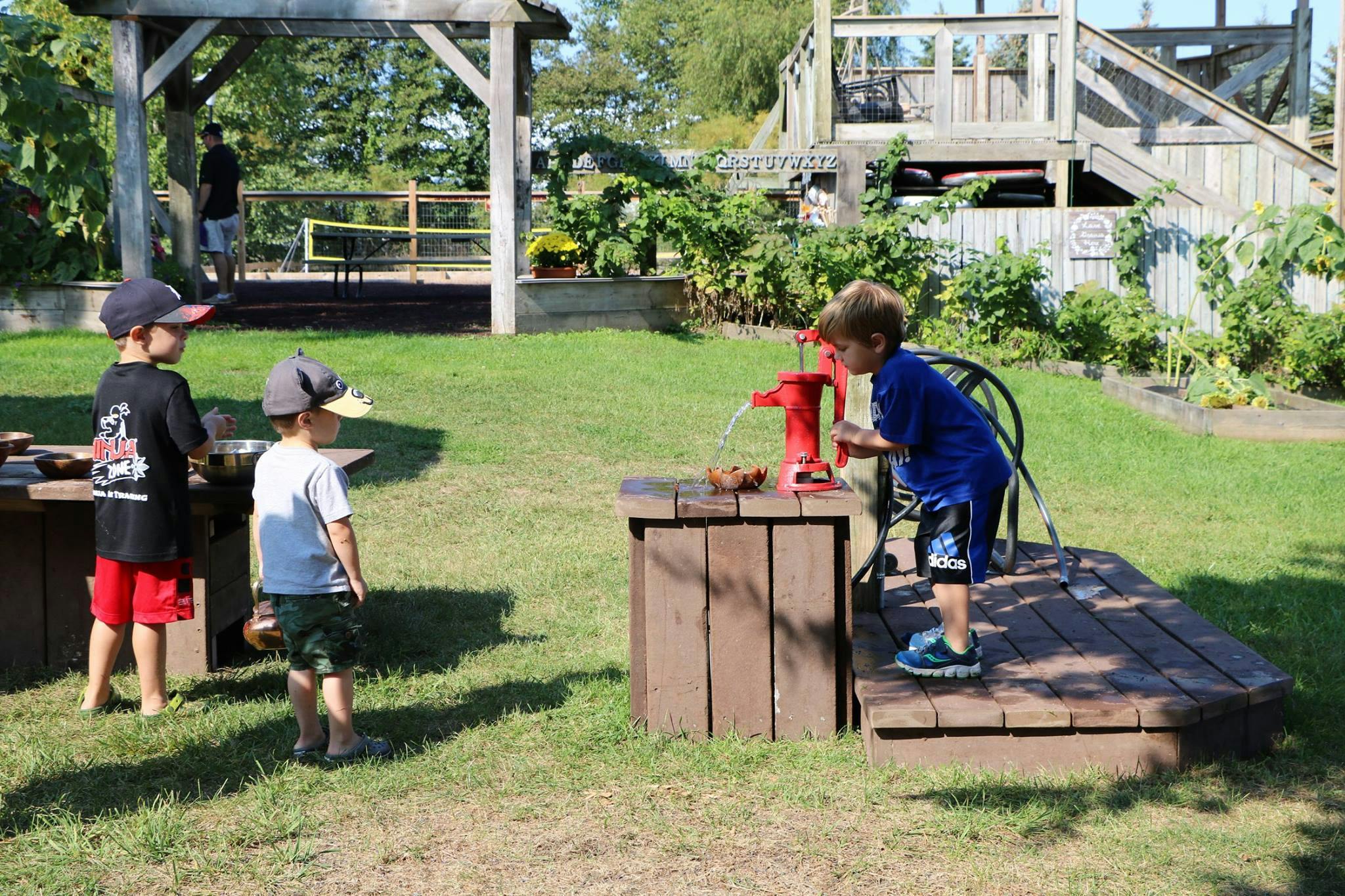 Child playing with a water pump while two other children watch