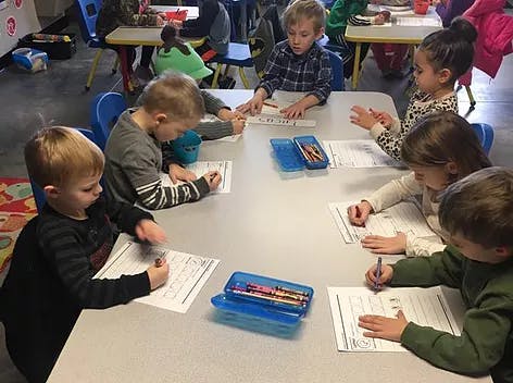 Children sitting at a table writing on papers in a classroom