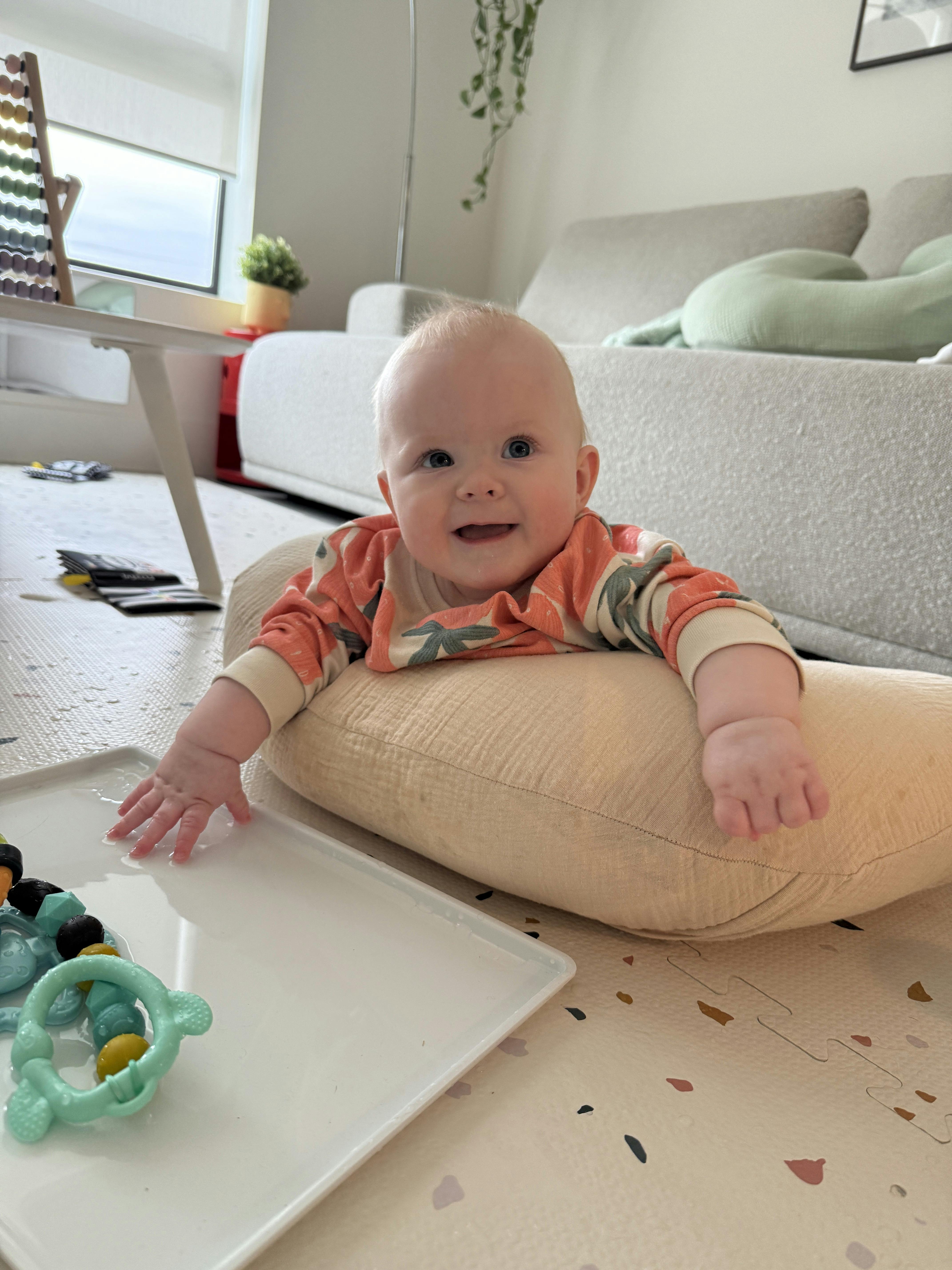 Child on a pillow on the floor reaching for a toy