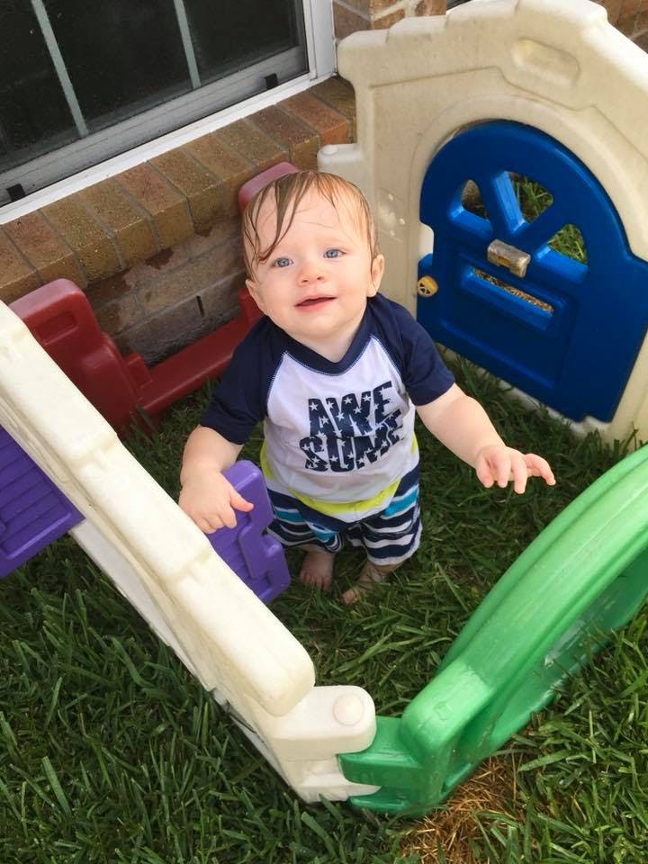 Child standing on grass next to a plastic play structure