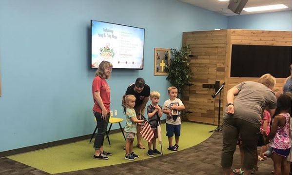 Adults and children standing in a room, some children holding flags