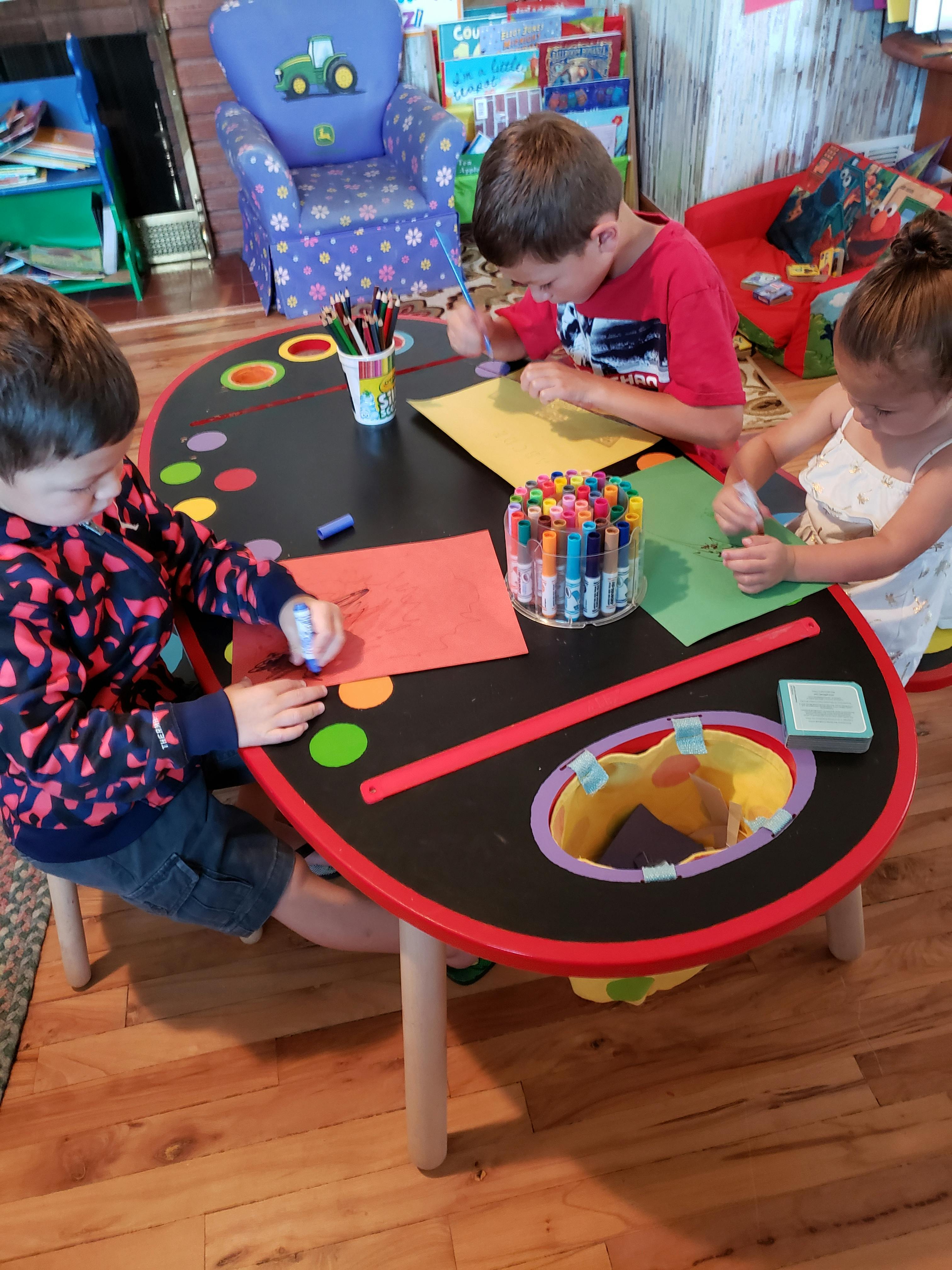 Three children drawing and coloring at a table