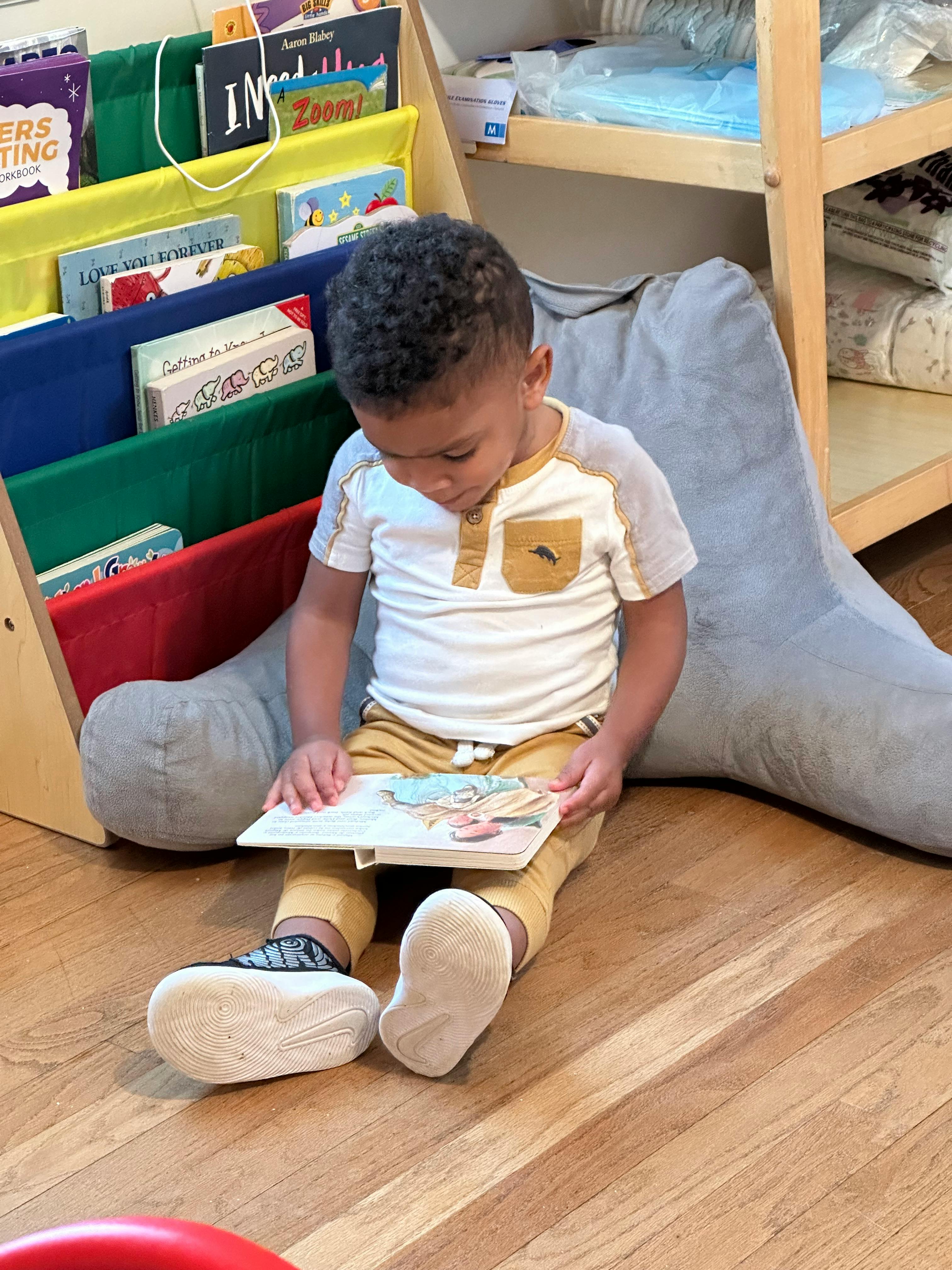 Child sitting on floor reading a book next to a bookshelf