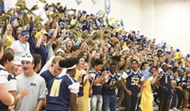 People in bleachers cheering with people in sports uniforms in foreground