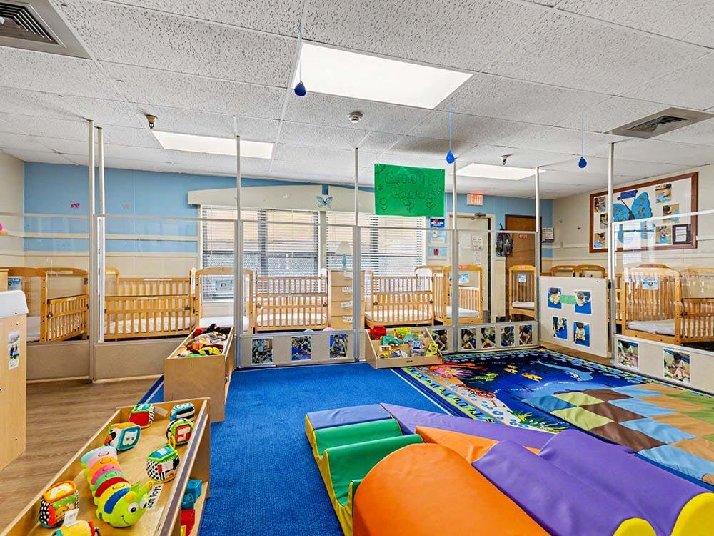 A colorful childcare room with cribs, play mats, and toys