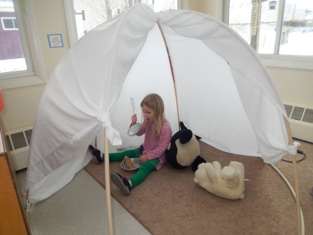 Child sitting inside a white fabric tent structure