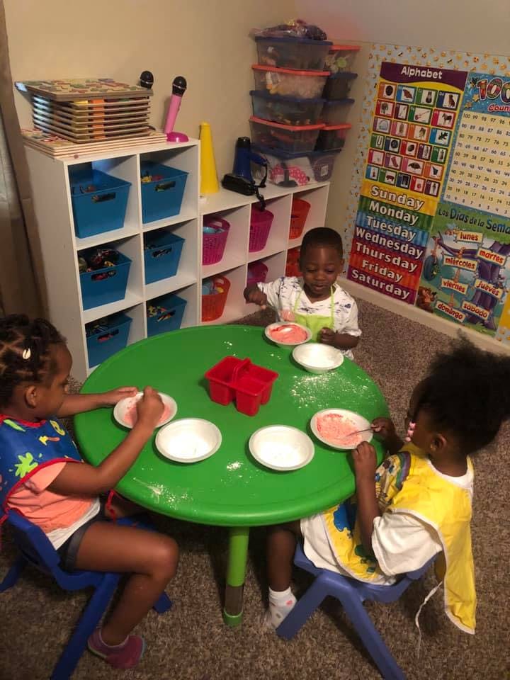 Three children sitting at a green table with bowls and spoons