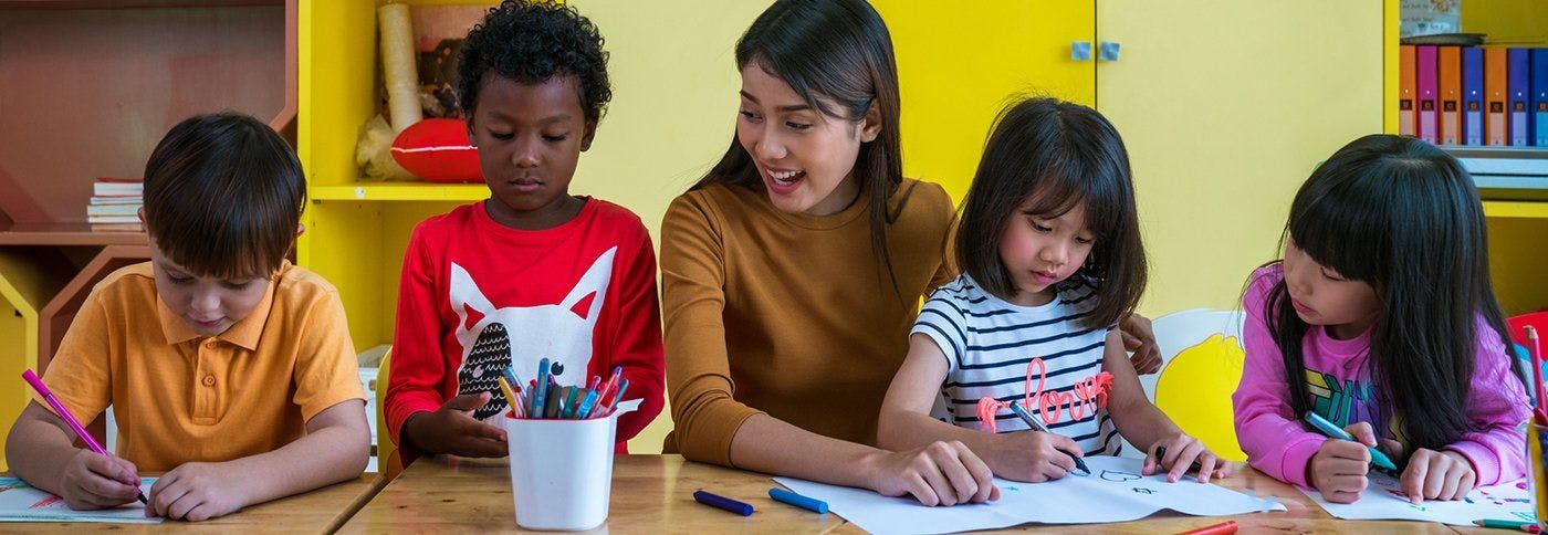Teacher and three children drawing in a classroom