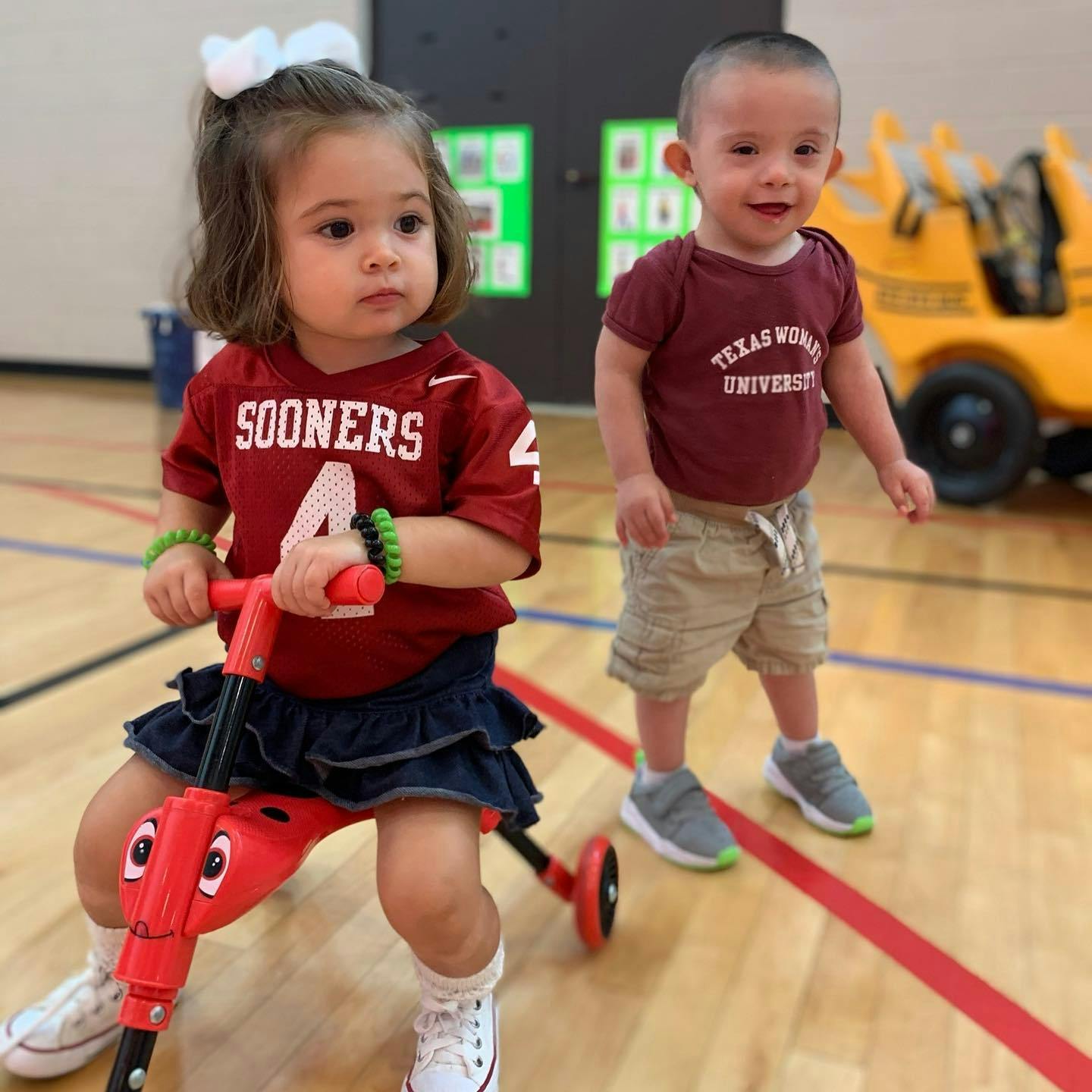 Child on a red scooter next to another child standing