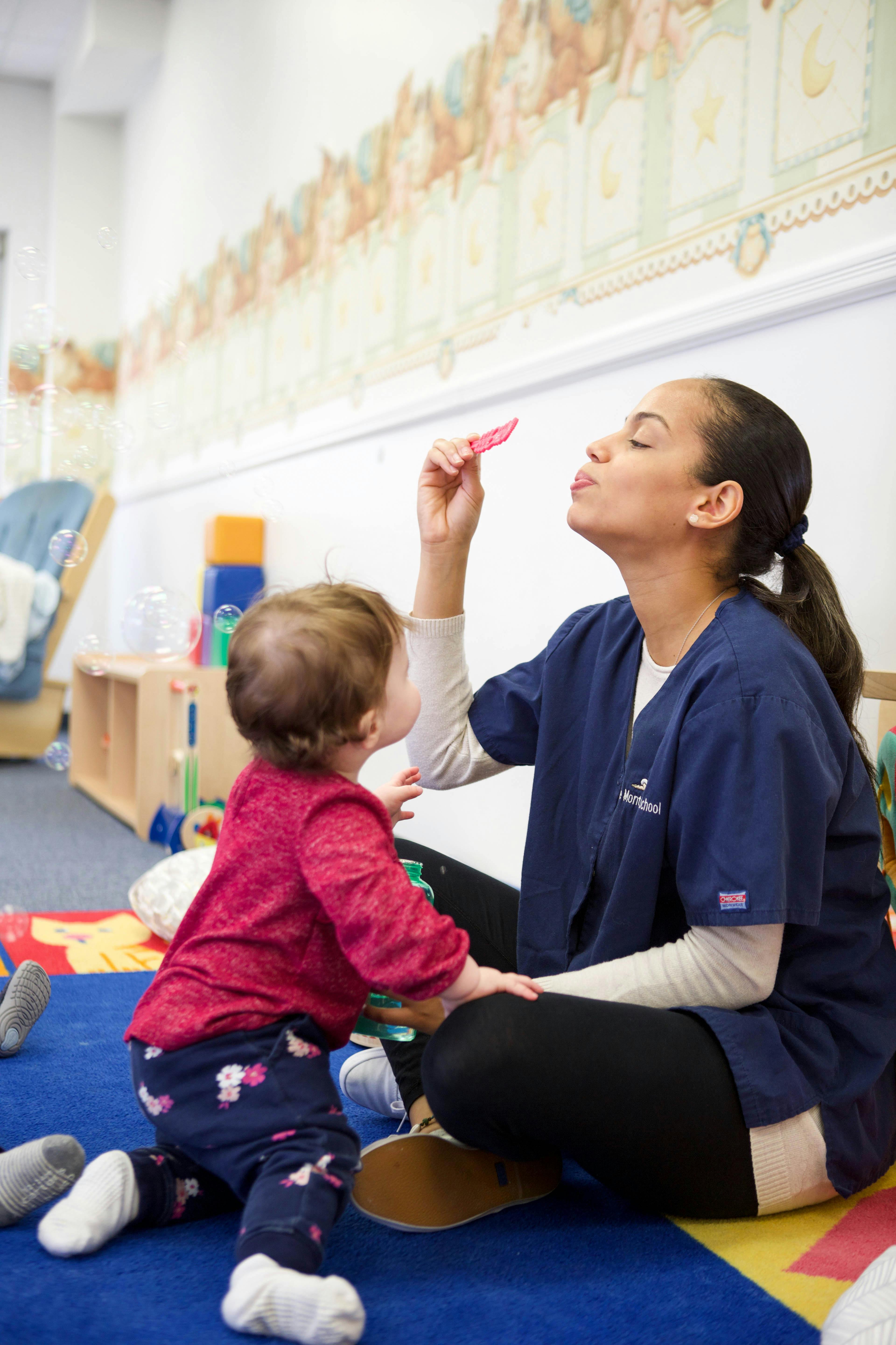 Person in scrubs blowing bubbles for a child