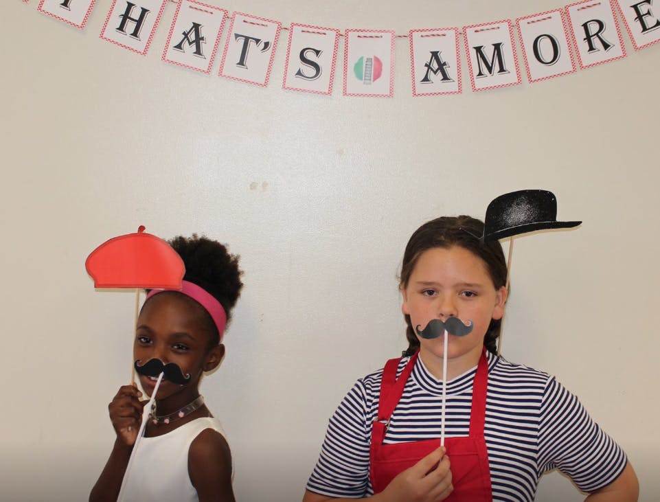 Two children holding up prop mustaches to their faces