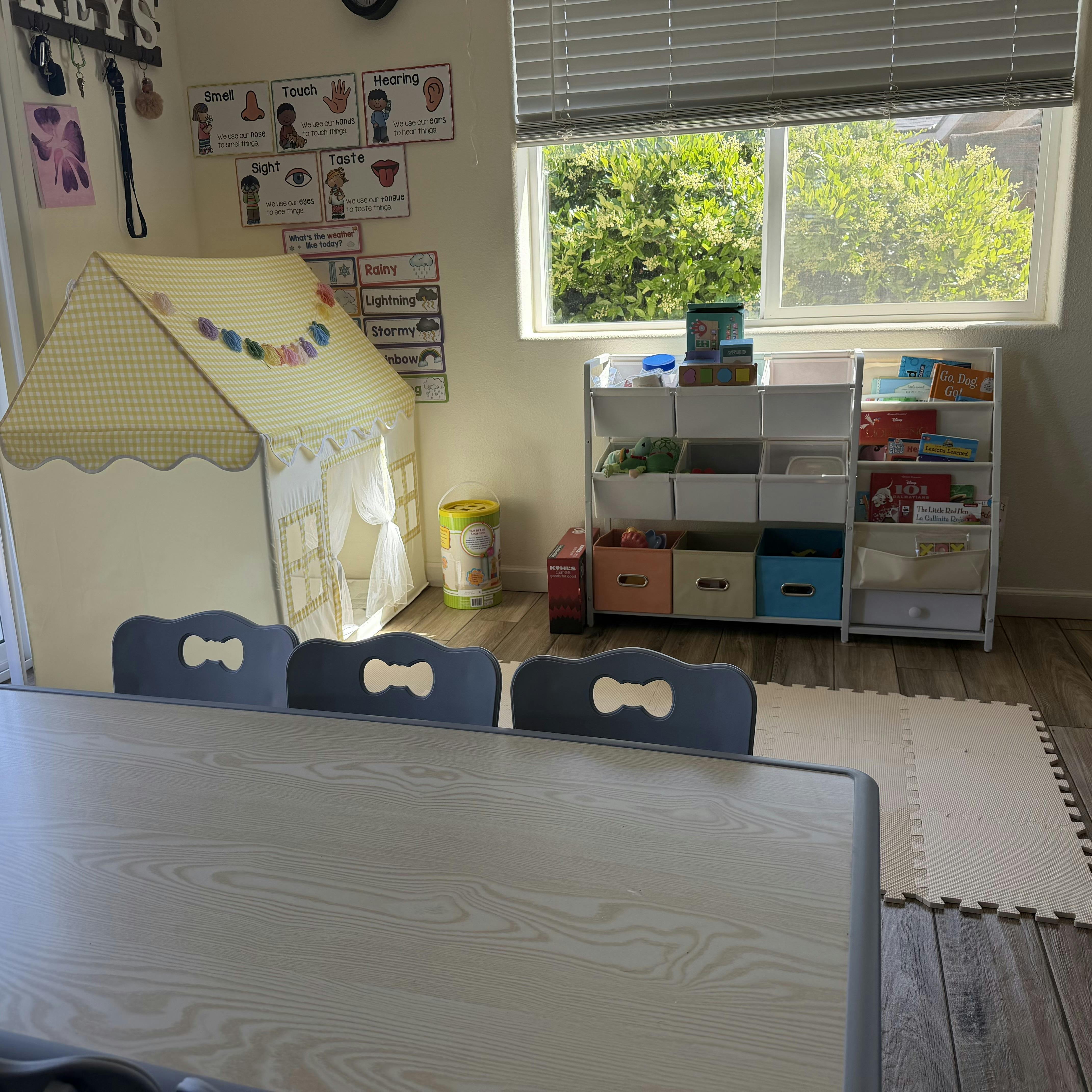 Classroom with play tent, storage unit with books and toys, and a table with chairs
