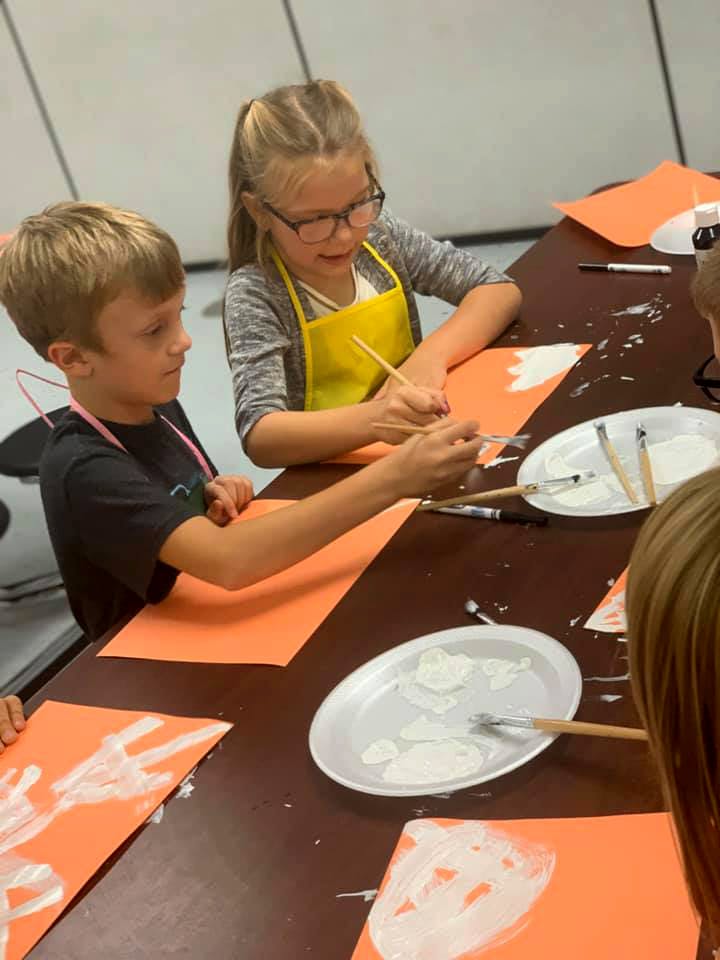 Two children painting on orange paper at a table