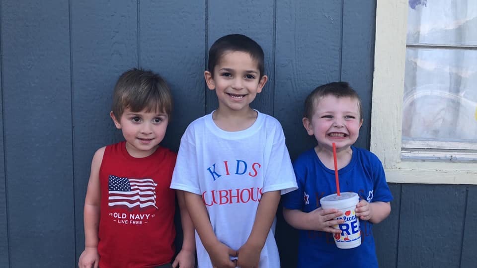 Three children standing together, one holding a drink