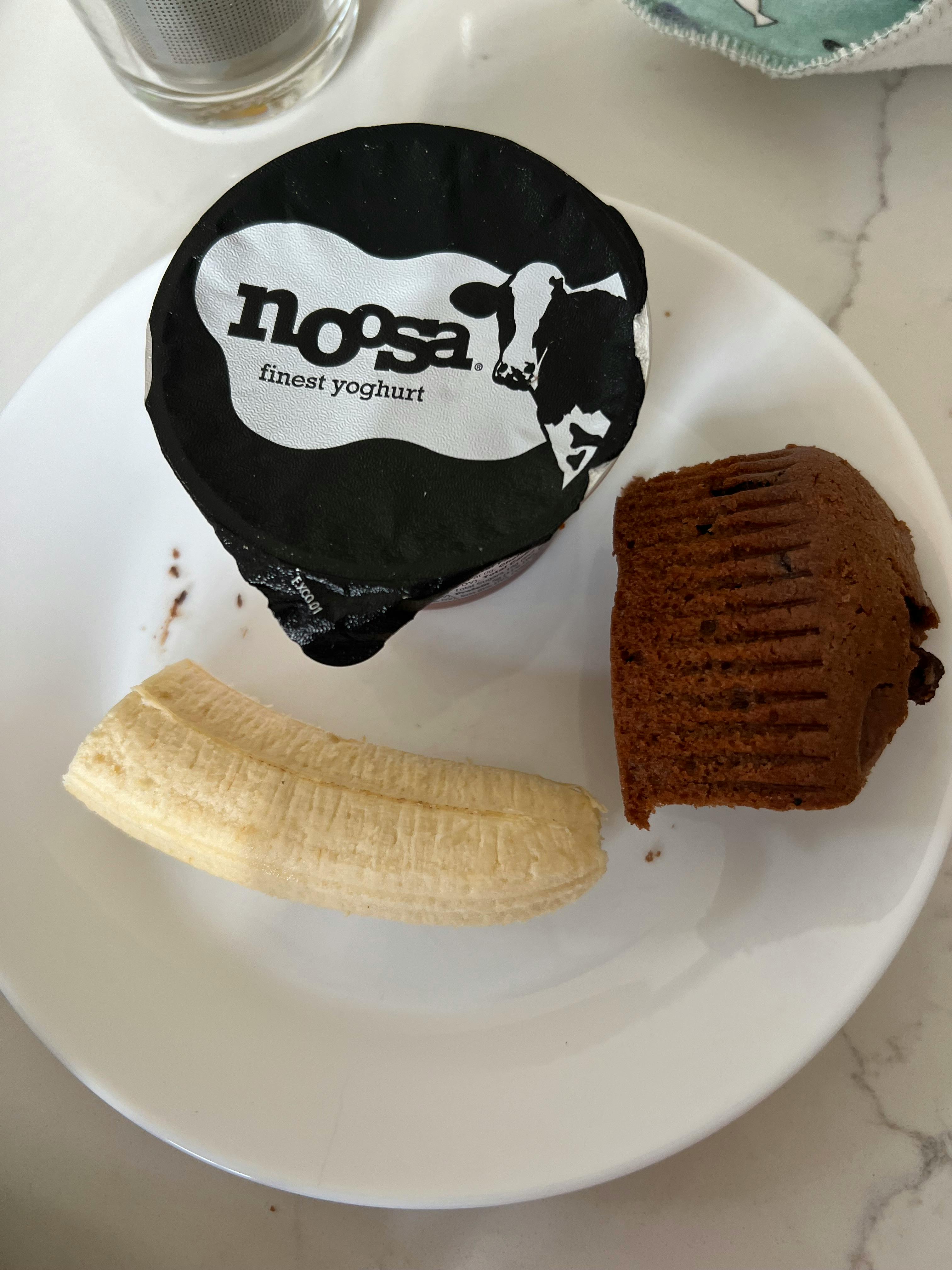 Yogurt container, peeled banana, and chocolate muffin on a plate