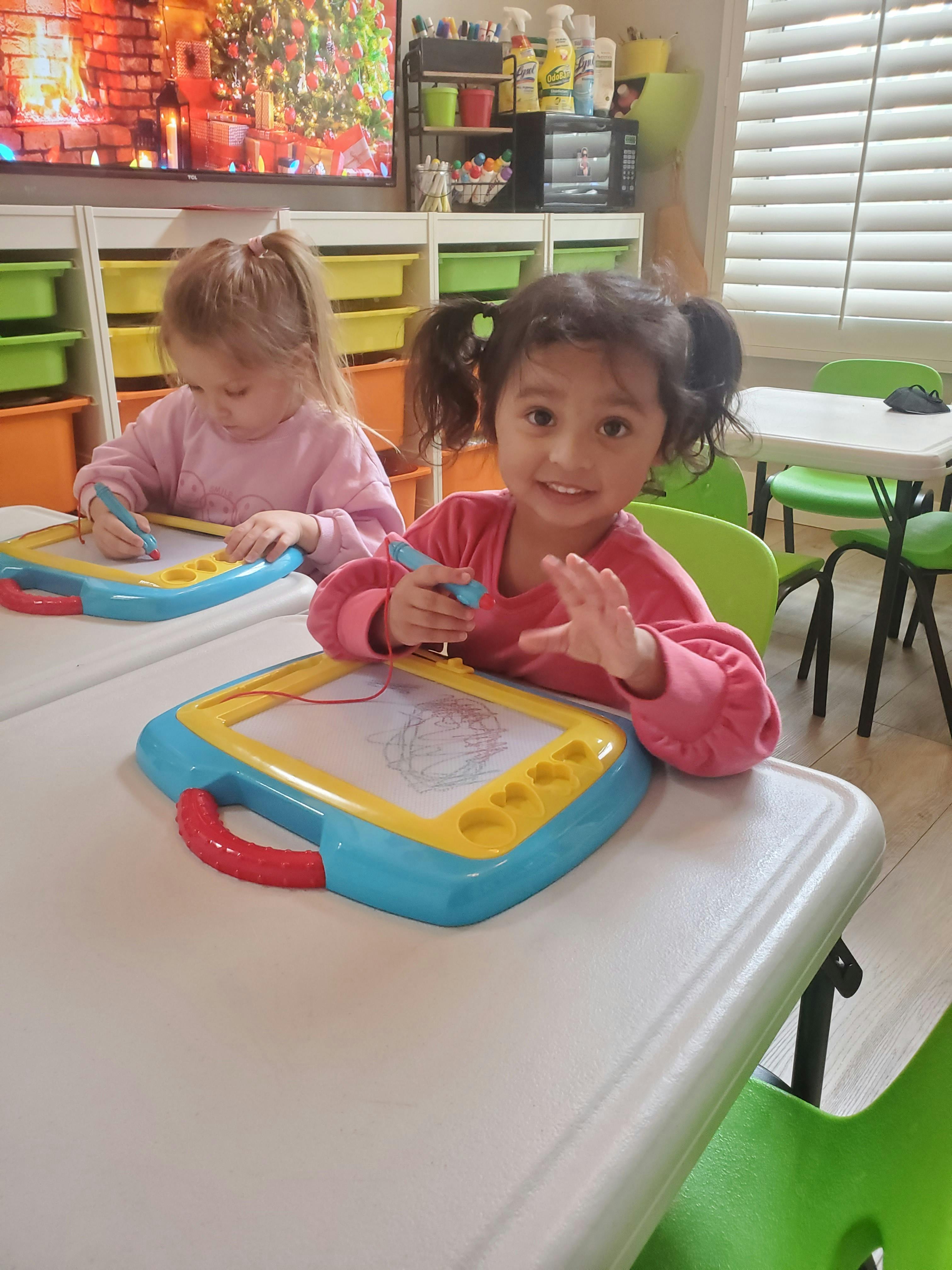 Two children sitting at a table drawing on magnetic writing pads
