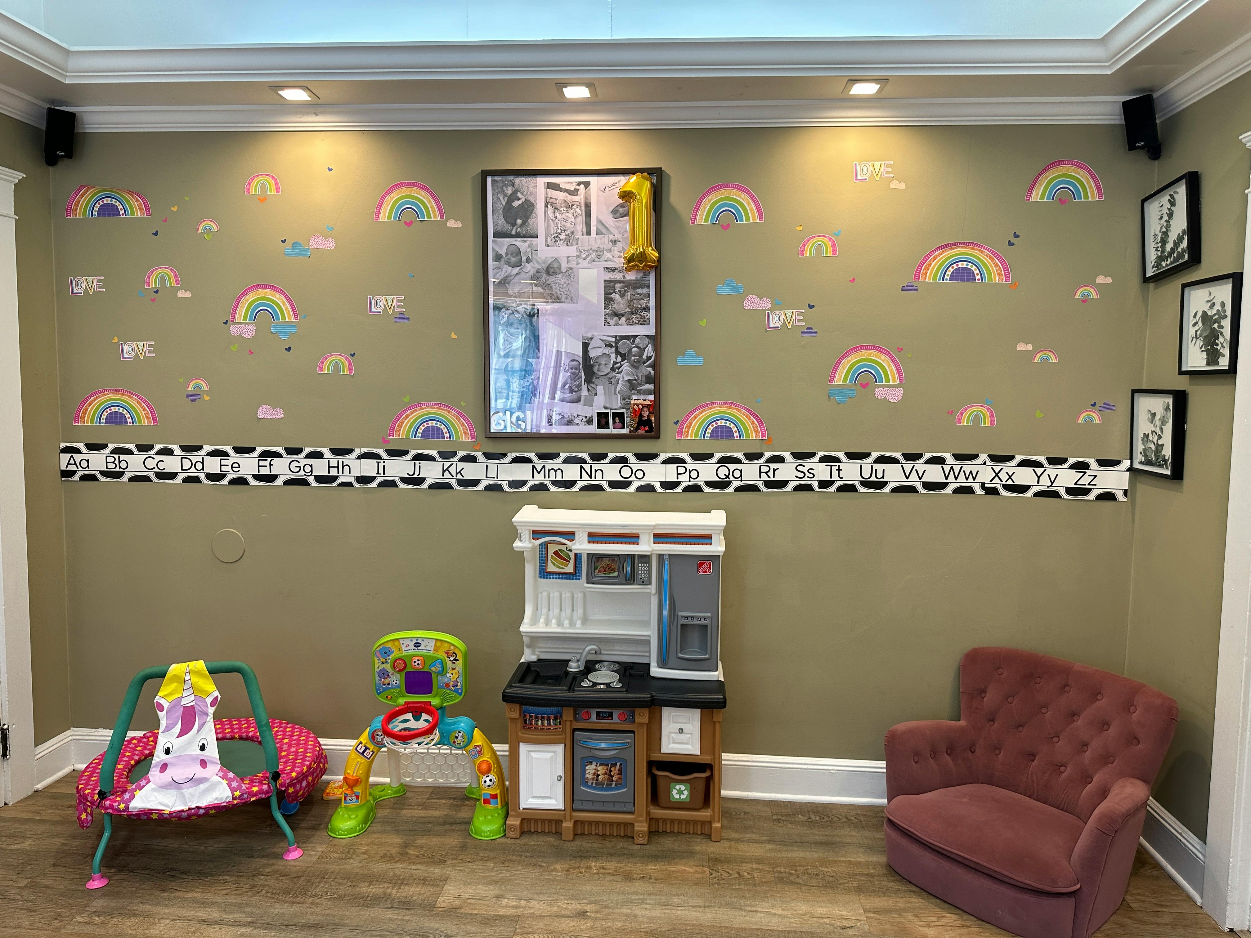 Playroom with rainbow wall decals, toy kitchen, and child's bouncer
