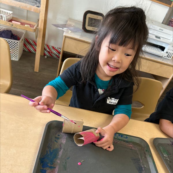 Child painting cardboard tubes at a table