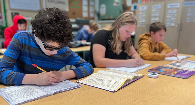 Students sitting at desks and writing in notebooks in a classroom
