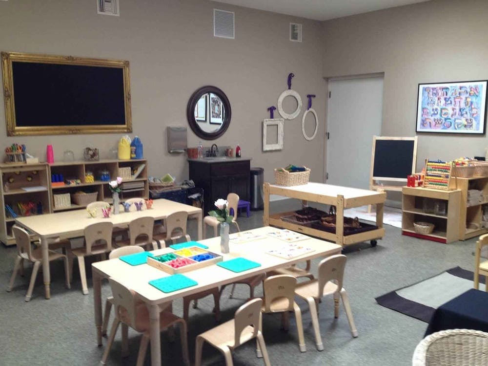 Classroom with small tables and chairs, shelves, and a large blackboard