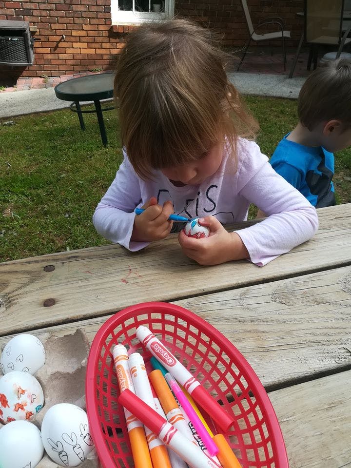 Child decorating an egg with a marker at a wooden table