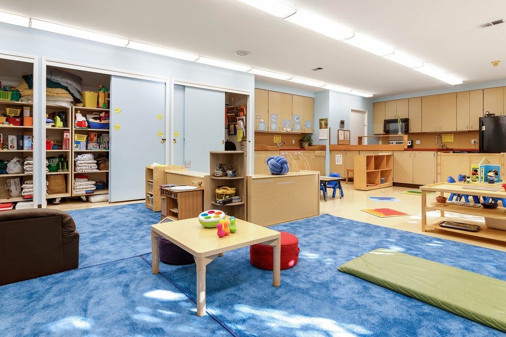 Children's classroom with a blue rug, small tables, and storage cubbies
