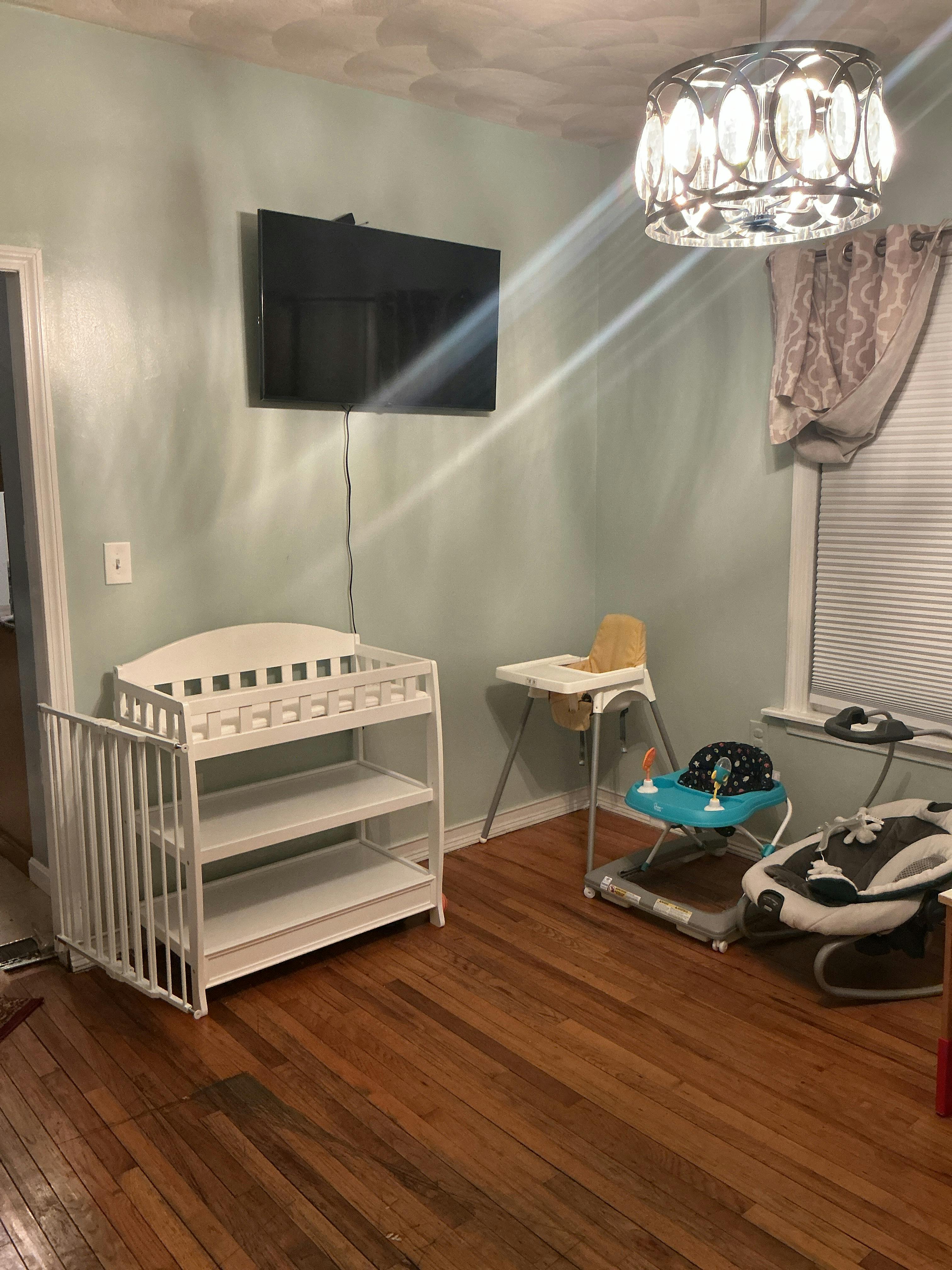 Baby changing table and high chair in a room with hardwood floors and a TV