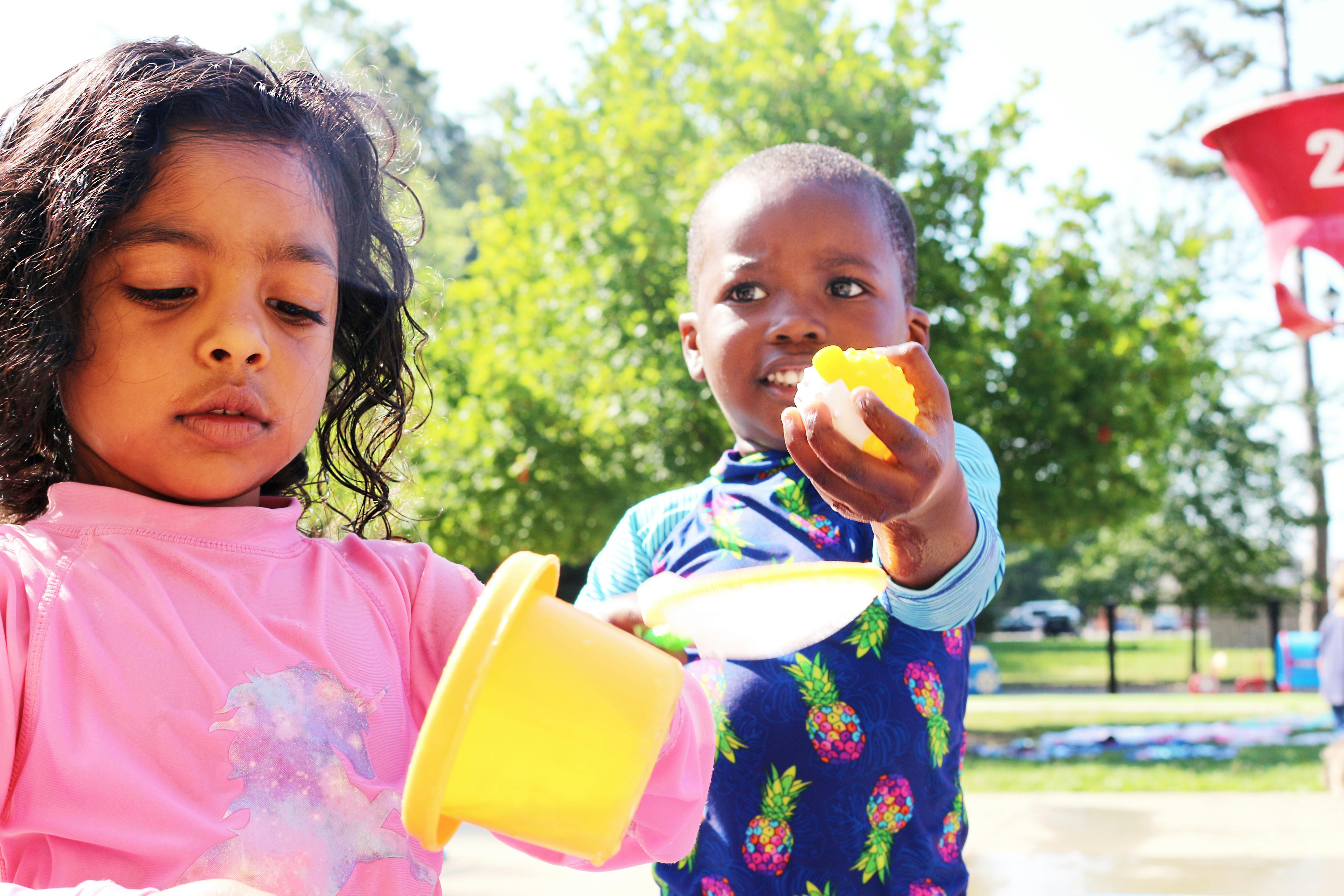 Two children playing with yellow sand toys outdoors