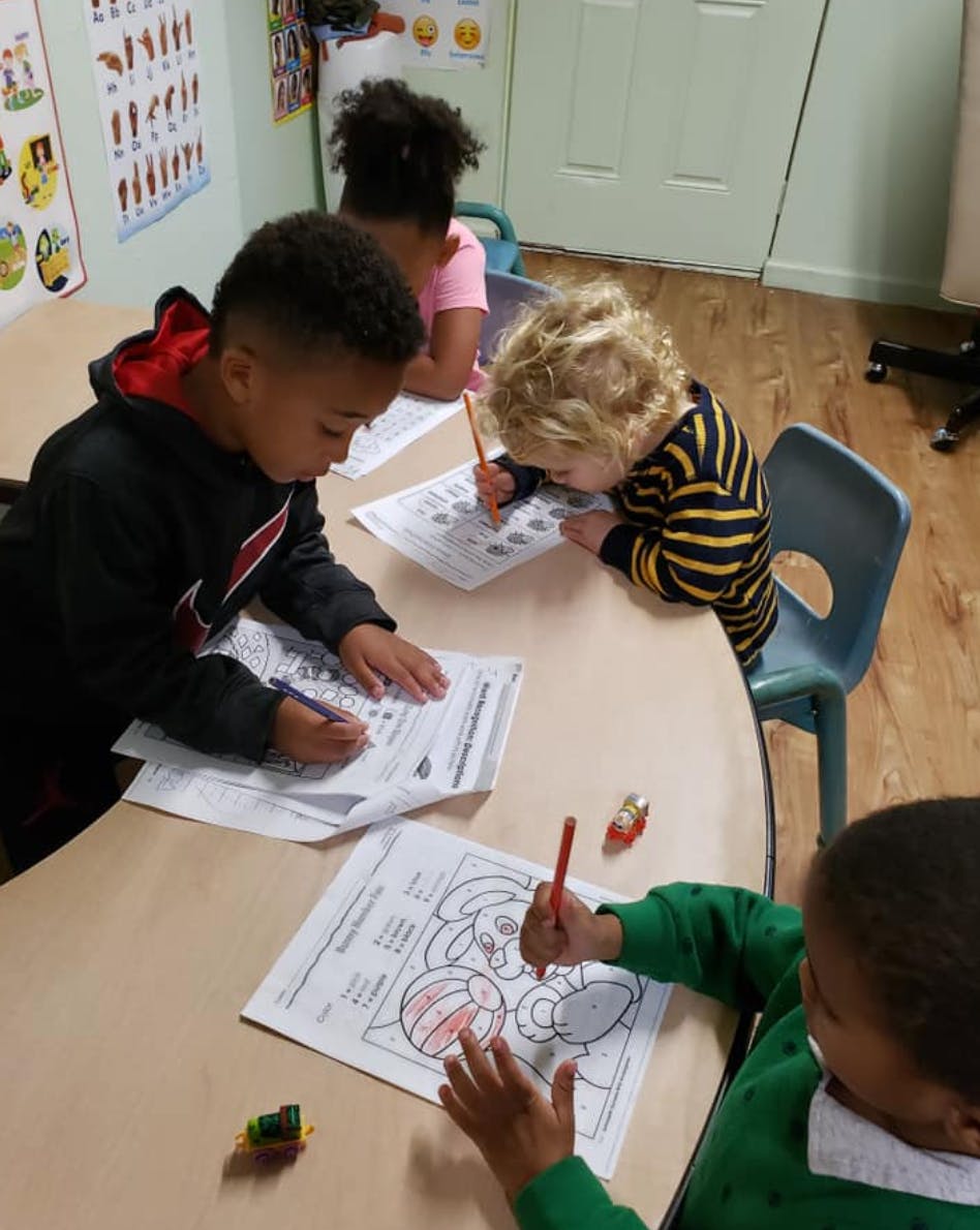 Children coloring and writing at a table in a classroom