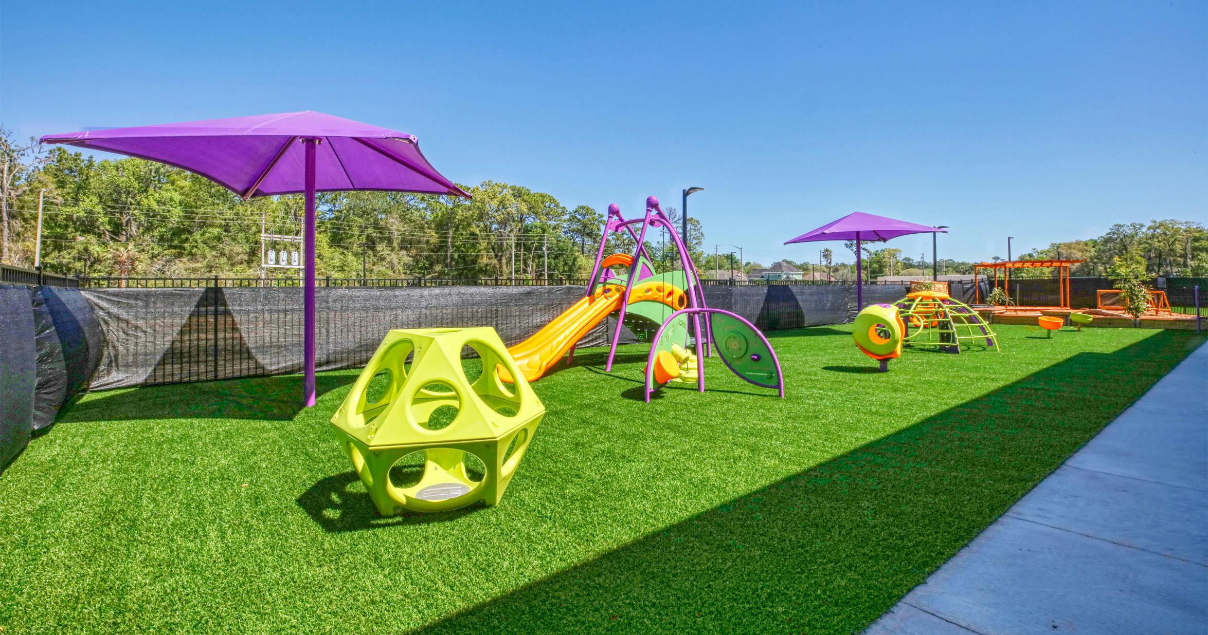 A colorful outdoor playground with slides, climbing structures, and purple umbrellas