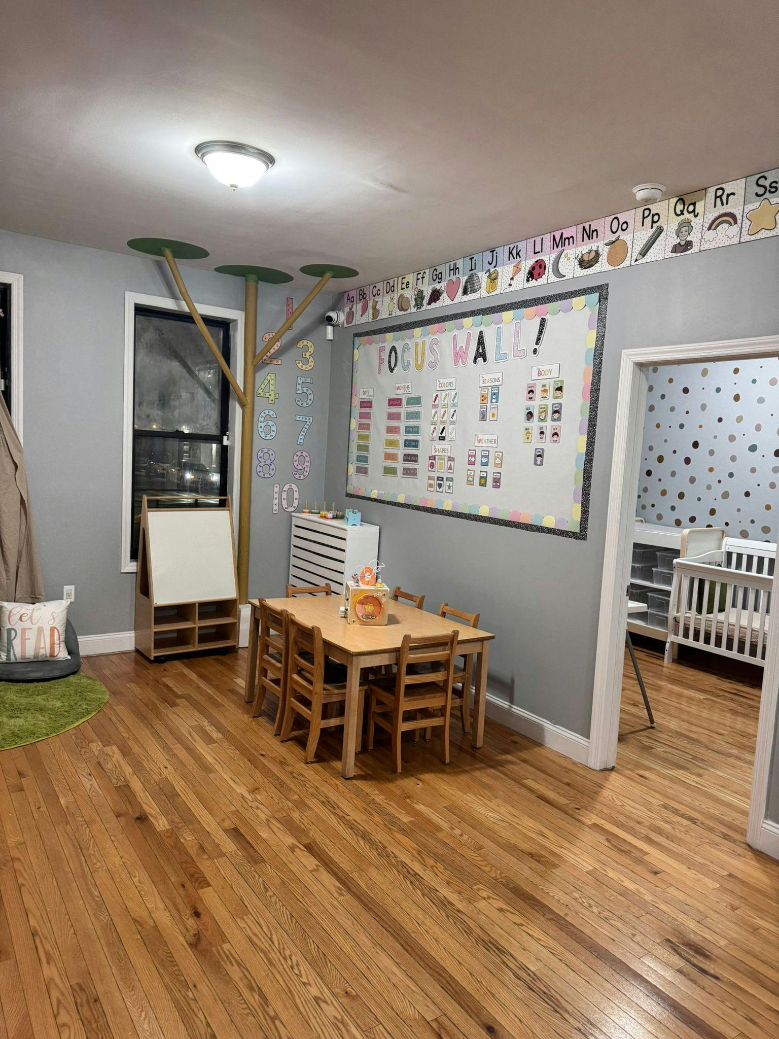Classroom with small table and chairs, whiteboard, and crib in adjacent room