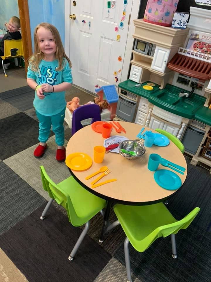 Child standing next to a small table with toy dishes