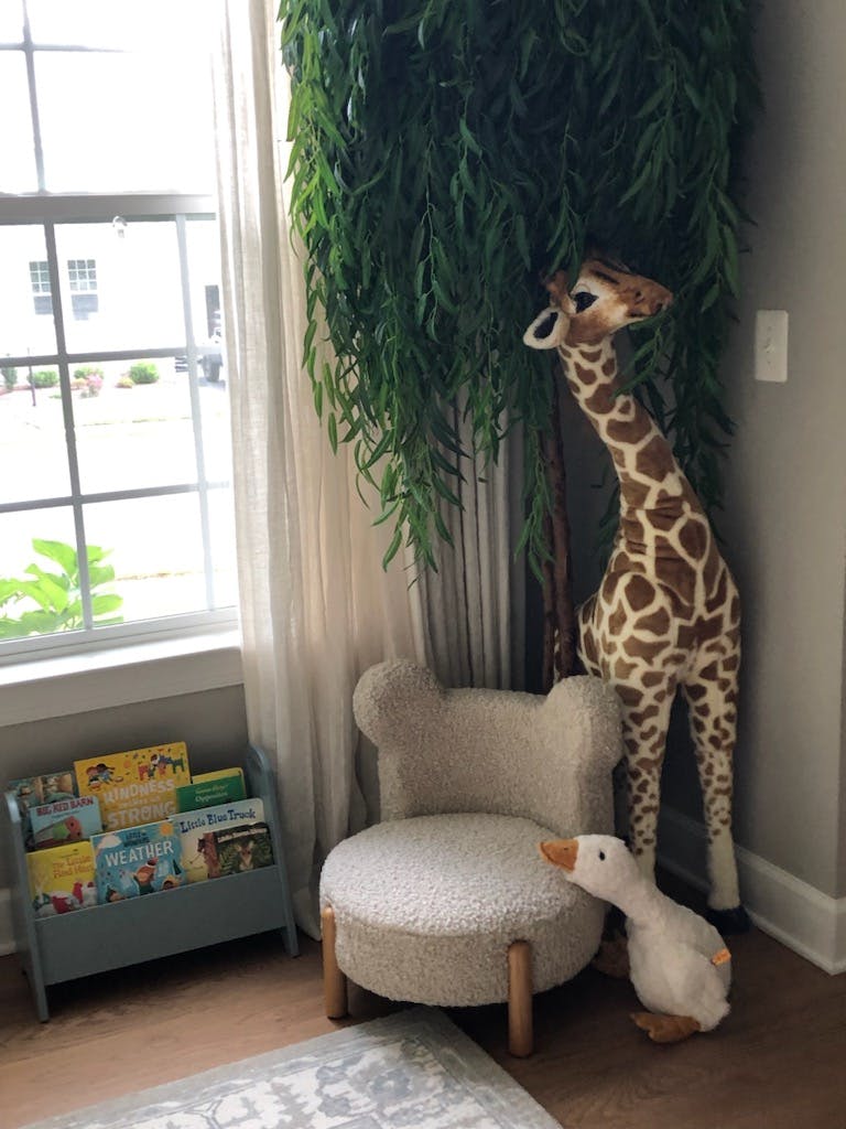 Stuffed giraffe and goose next to a small chair and bookshelf