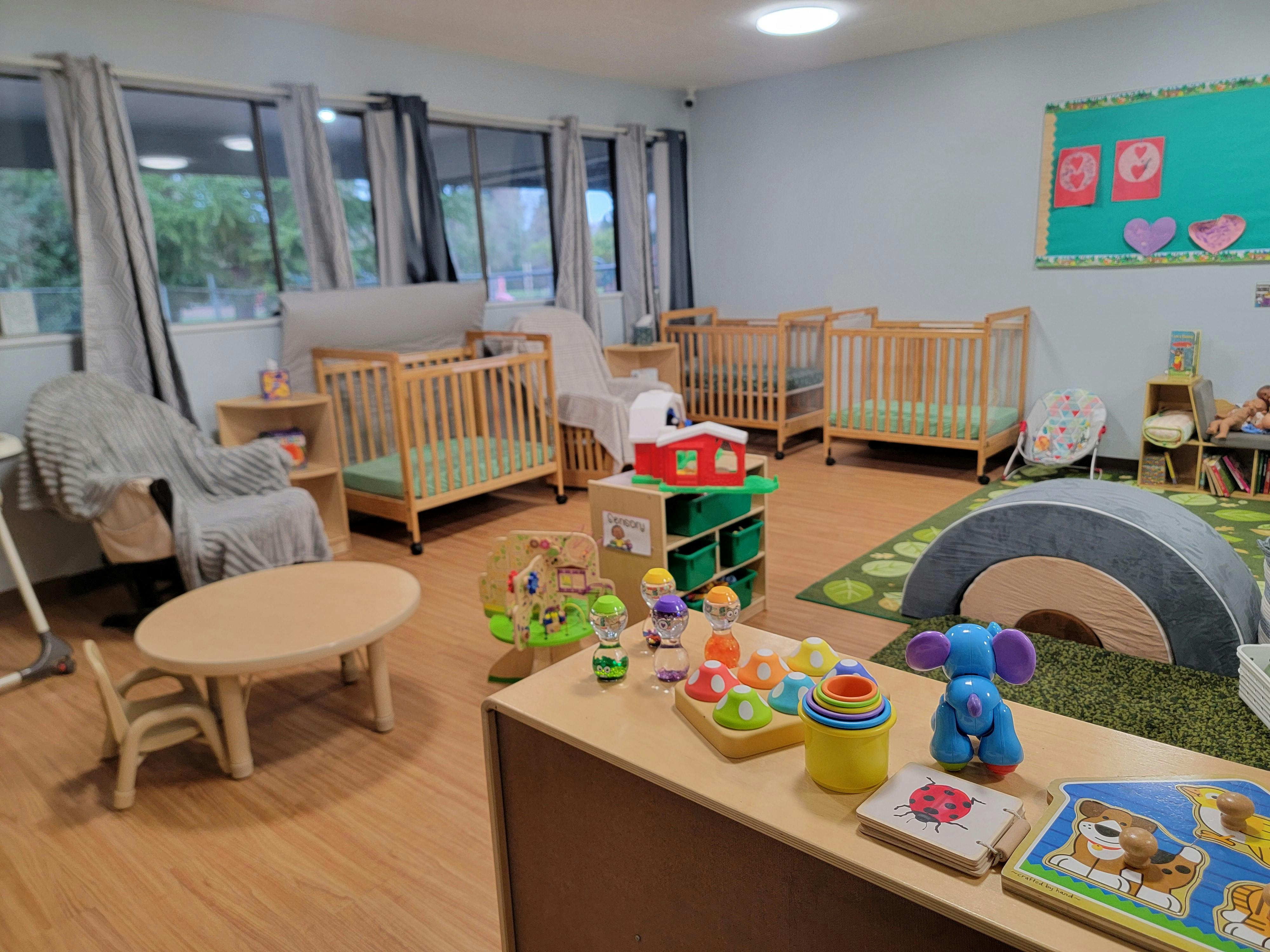 A room with multiple cribs, a small table and chair, and various toys