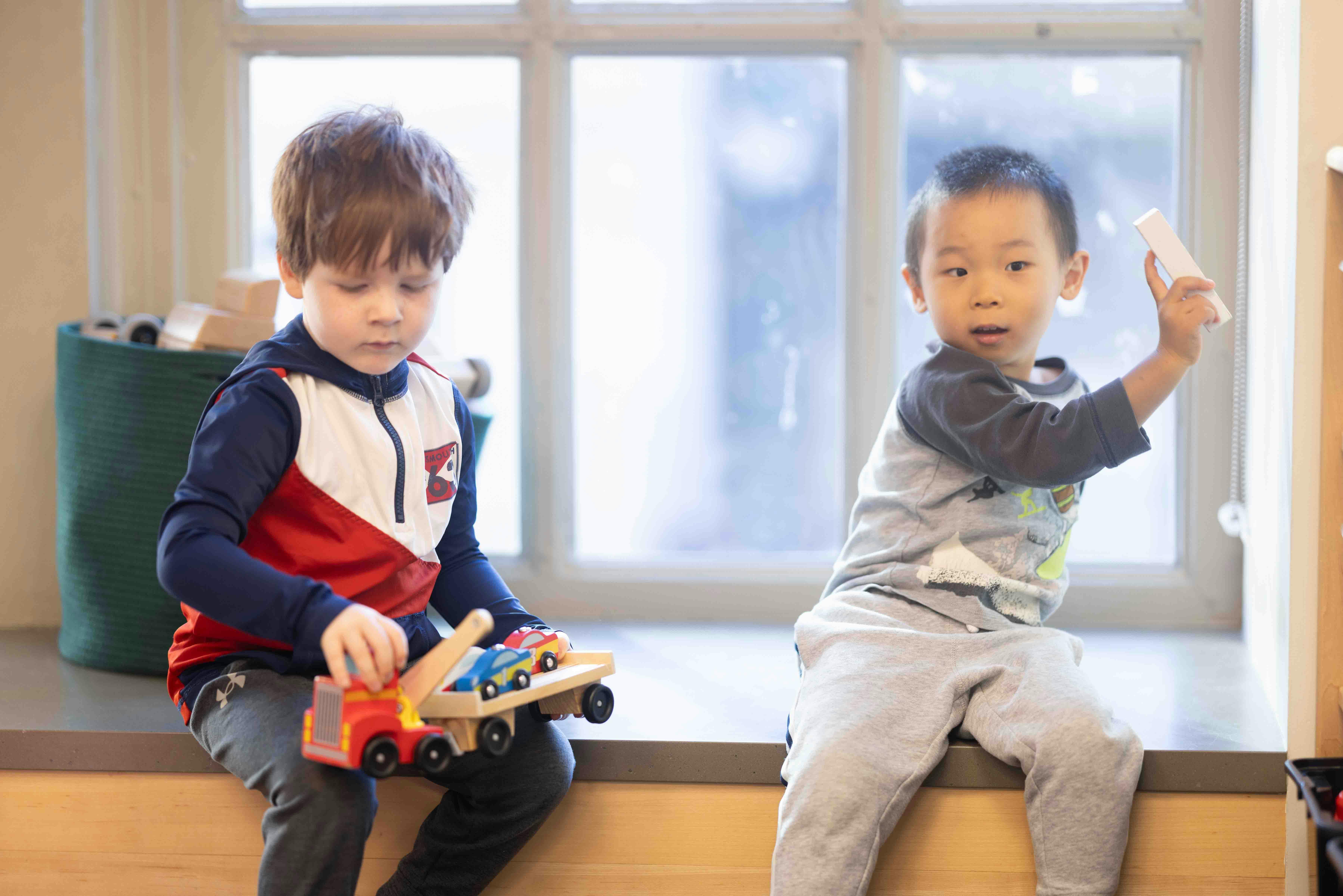 Two young children playing with toys on a window ledge