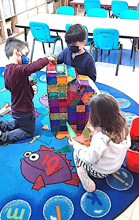 Three children playing with colorful magnetic building blocks on a rug