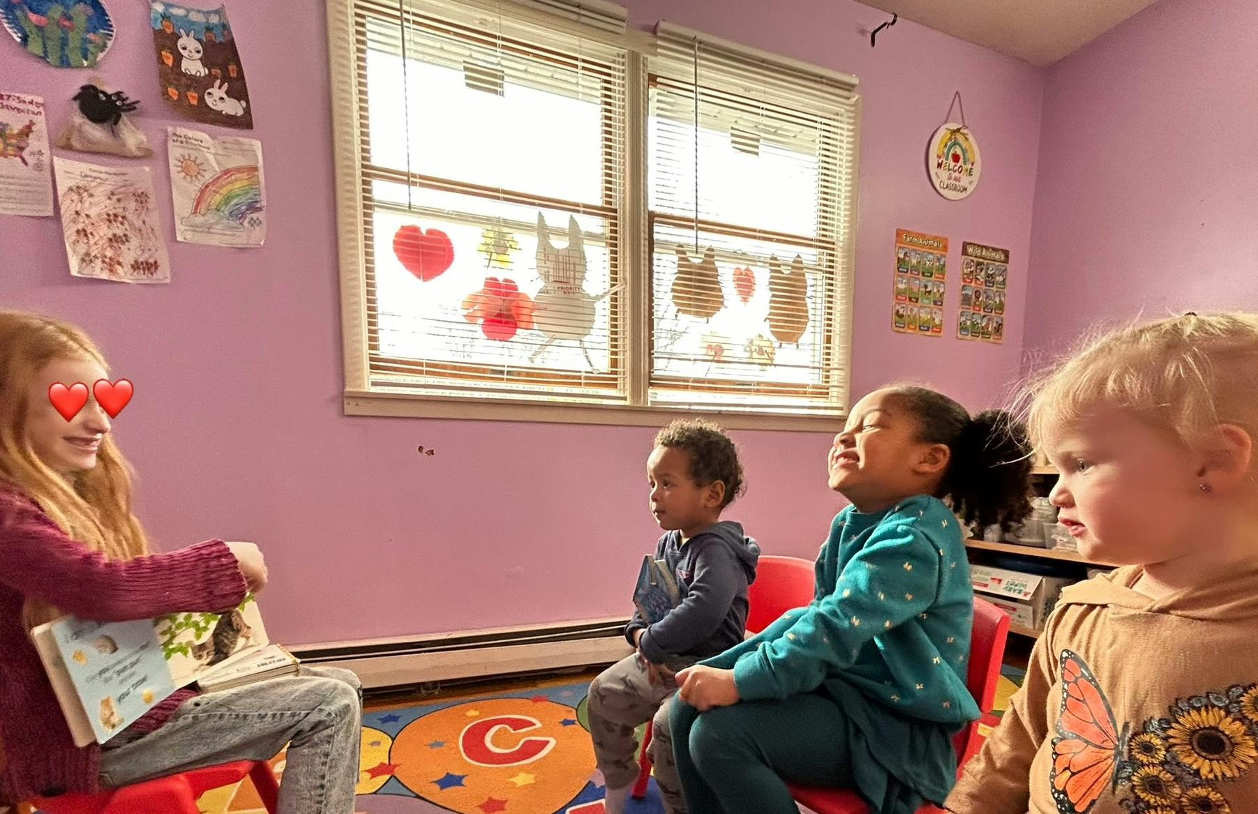 Teen reading a book to three children in a classroom