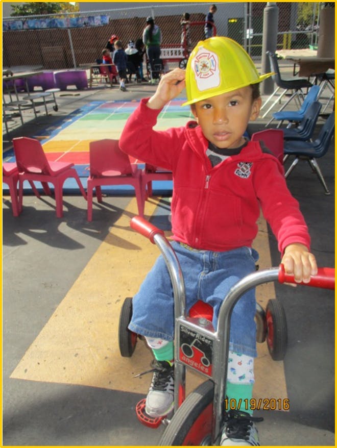 Child in a yellow hard hat on a tricycle