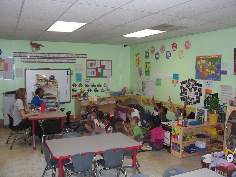 Children sitting on the floor in a classroom with some raising their hands
