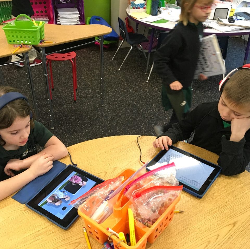 Two children using tablets at a table in a classroom