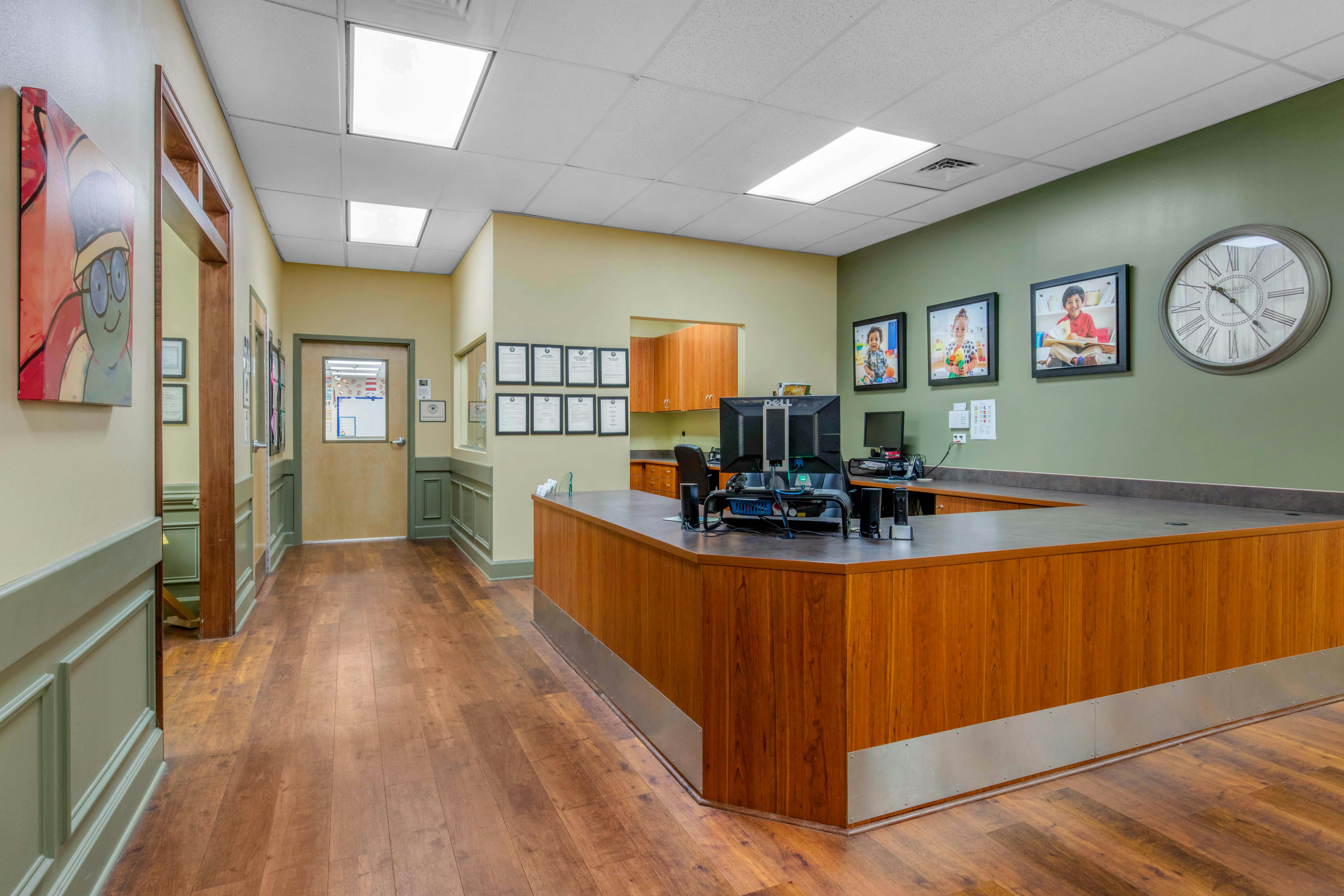 Reception desk with wood panels and gray counter, computers, and framed photos of children