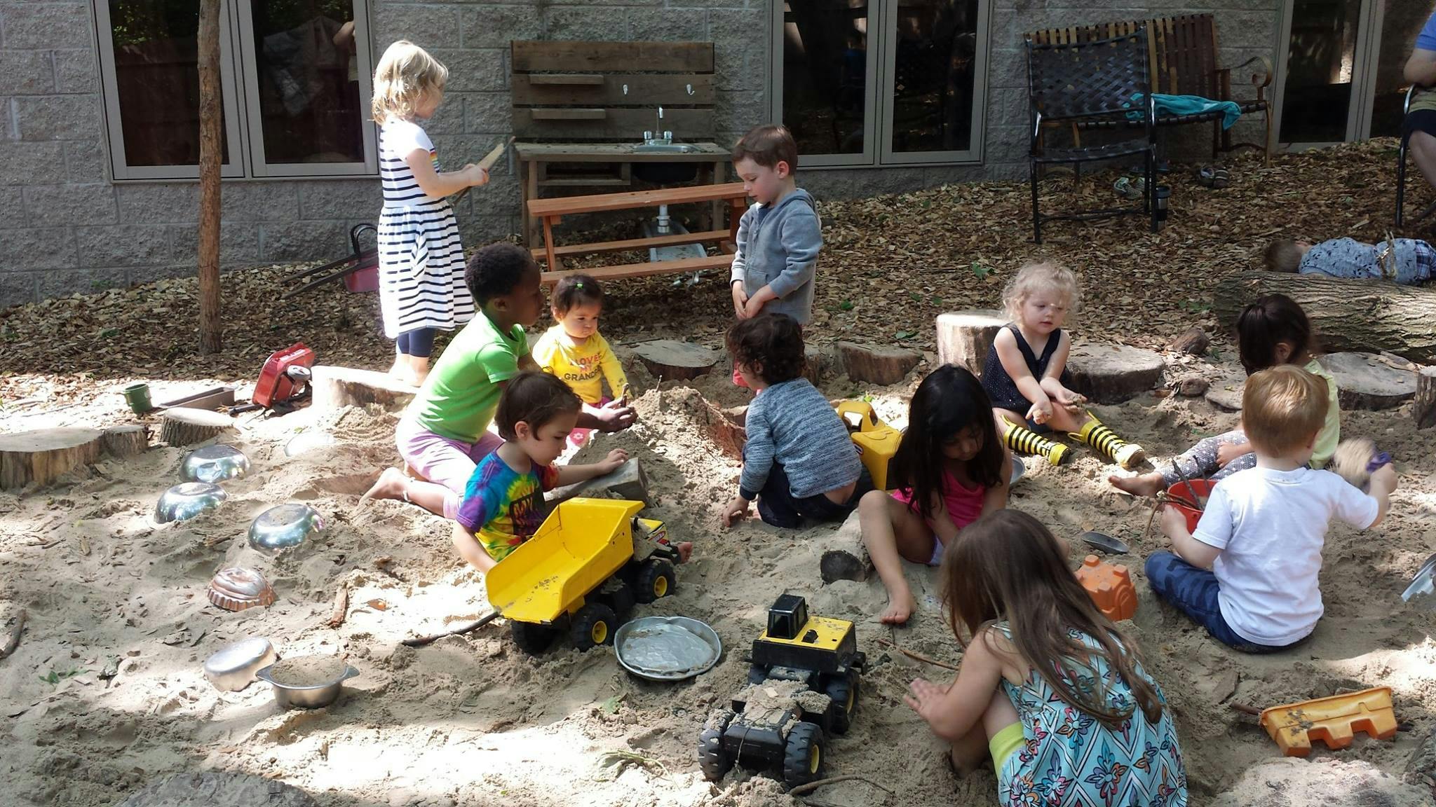 Adult and children playing in a sandbox with toys