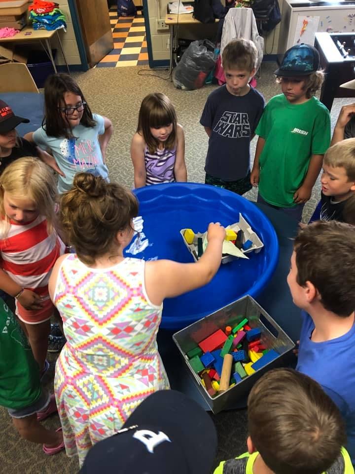 Adult and children gathered around a blue bin with floating objects