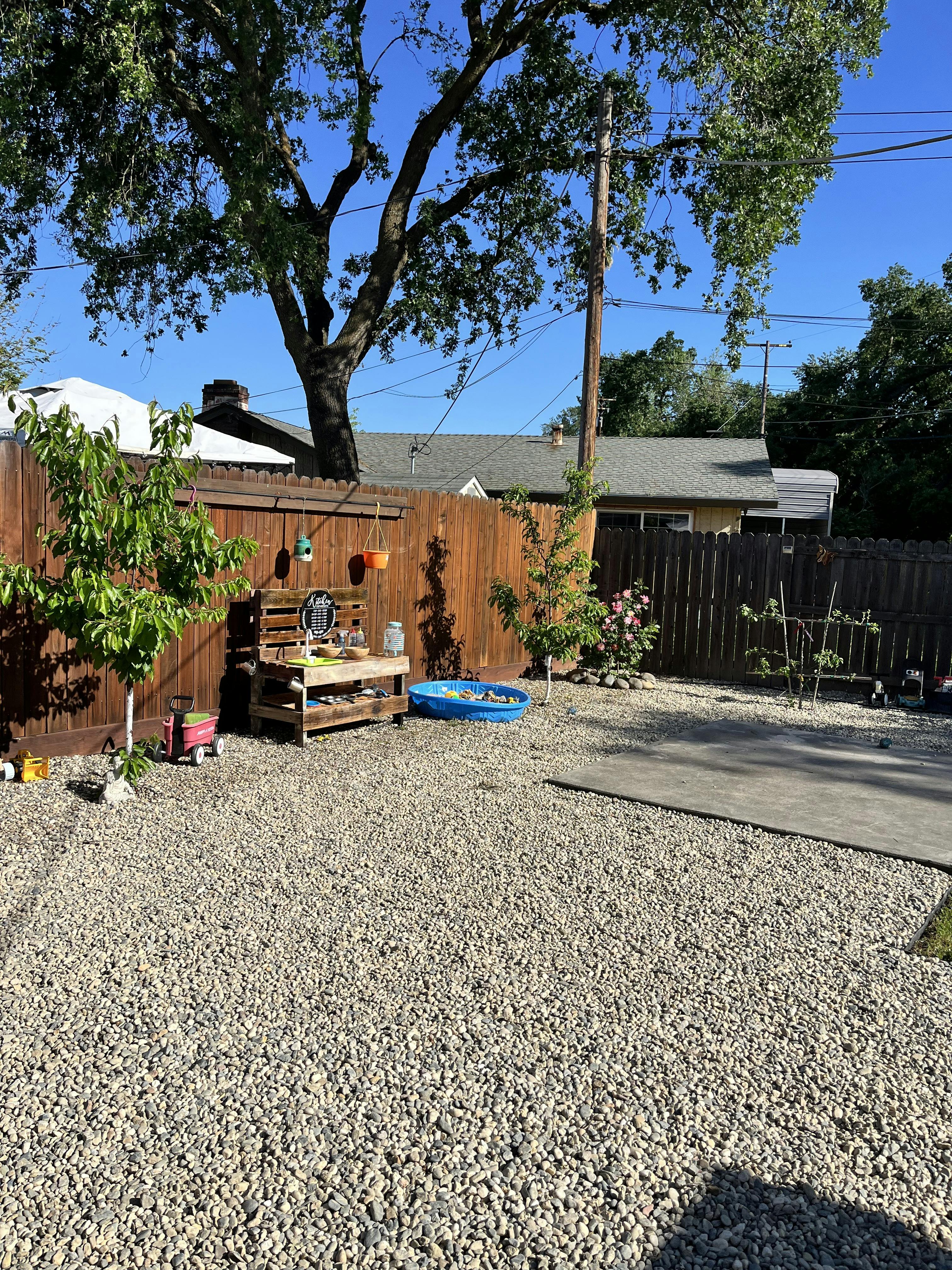 Gravel backyard with a wooden fence, small table, and blue kiddie pool