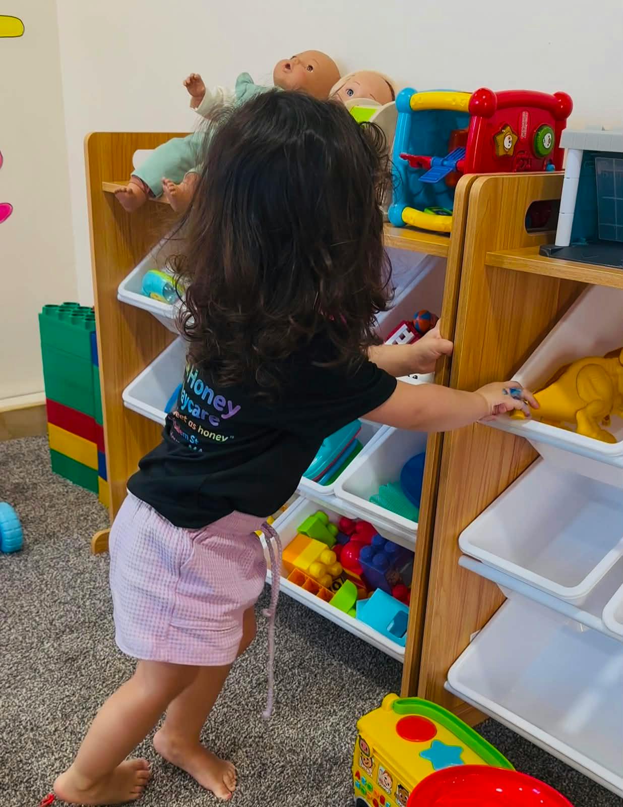 Child reaching into a toy shelf with various toys