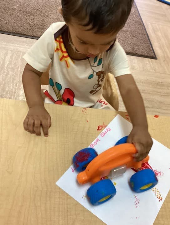 Child playing with a toy car on paper