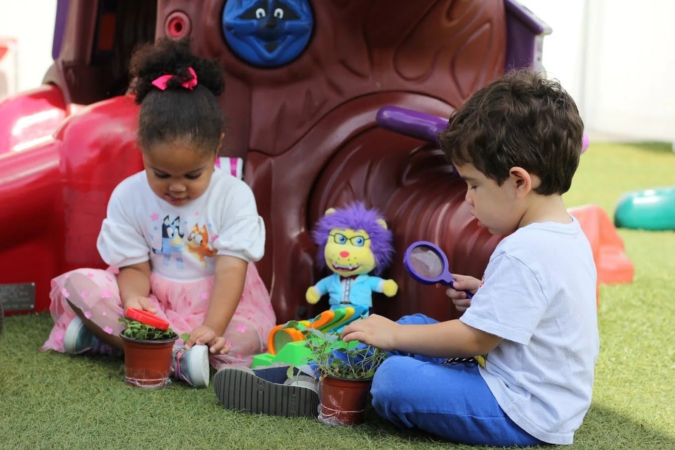 Two children playing with small potted plants and a magnifying glass